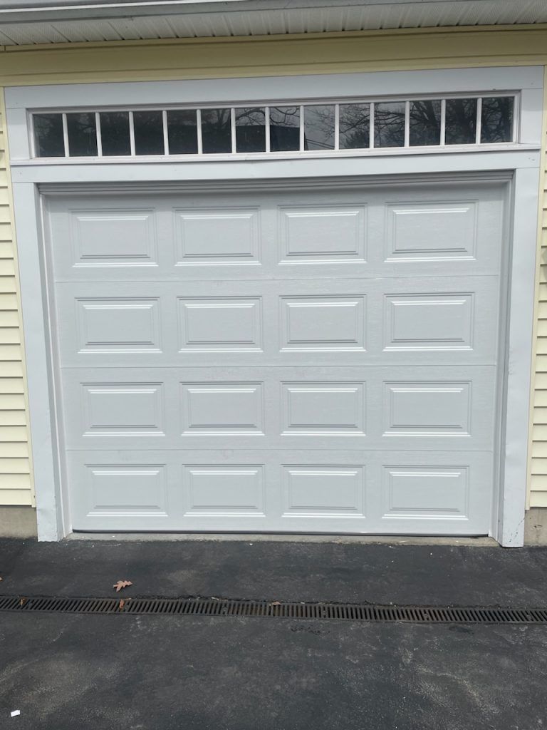 A white, four-panel residential garage door with a row of small, rectangular windows above it.