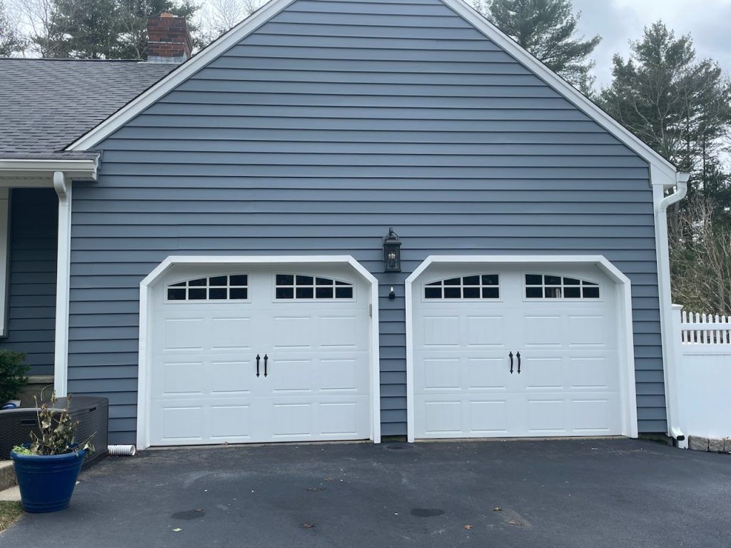A house exterior with two white arched garage doors under blue horizontal siding and a gray shingled roof.