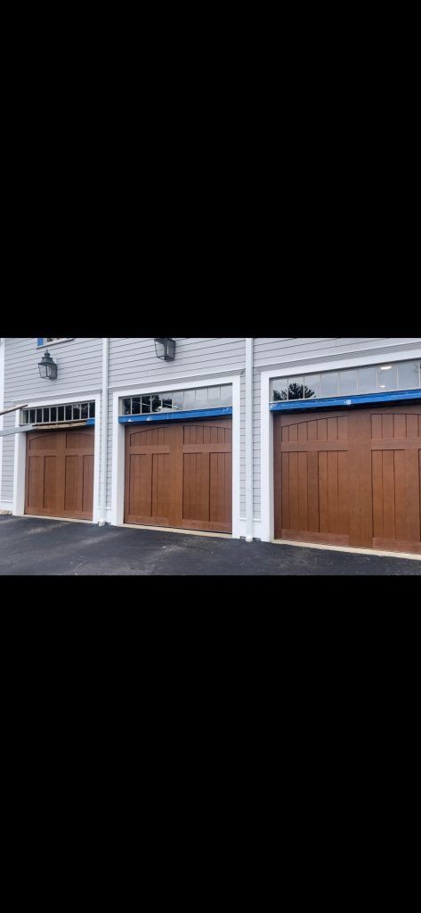 Three wood-toned garage doors with glass panel tops set against a grey-sided building.