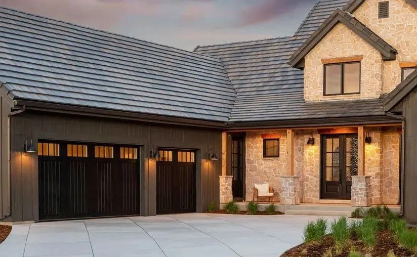 A two-story home with a dark gray shingled roof, stone exterior, and dark-toned garage doors and front entryway.