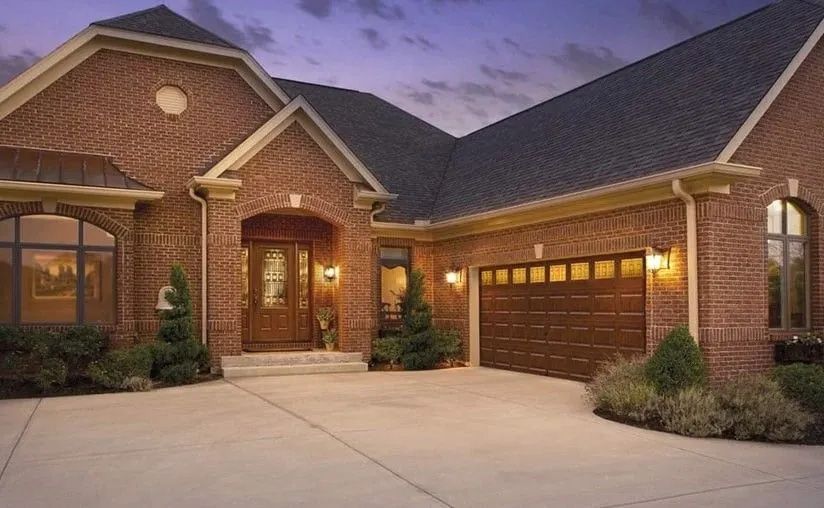 A red brick house with a dark roof and garage, featuring a front door under an arched entry at dusk.