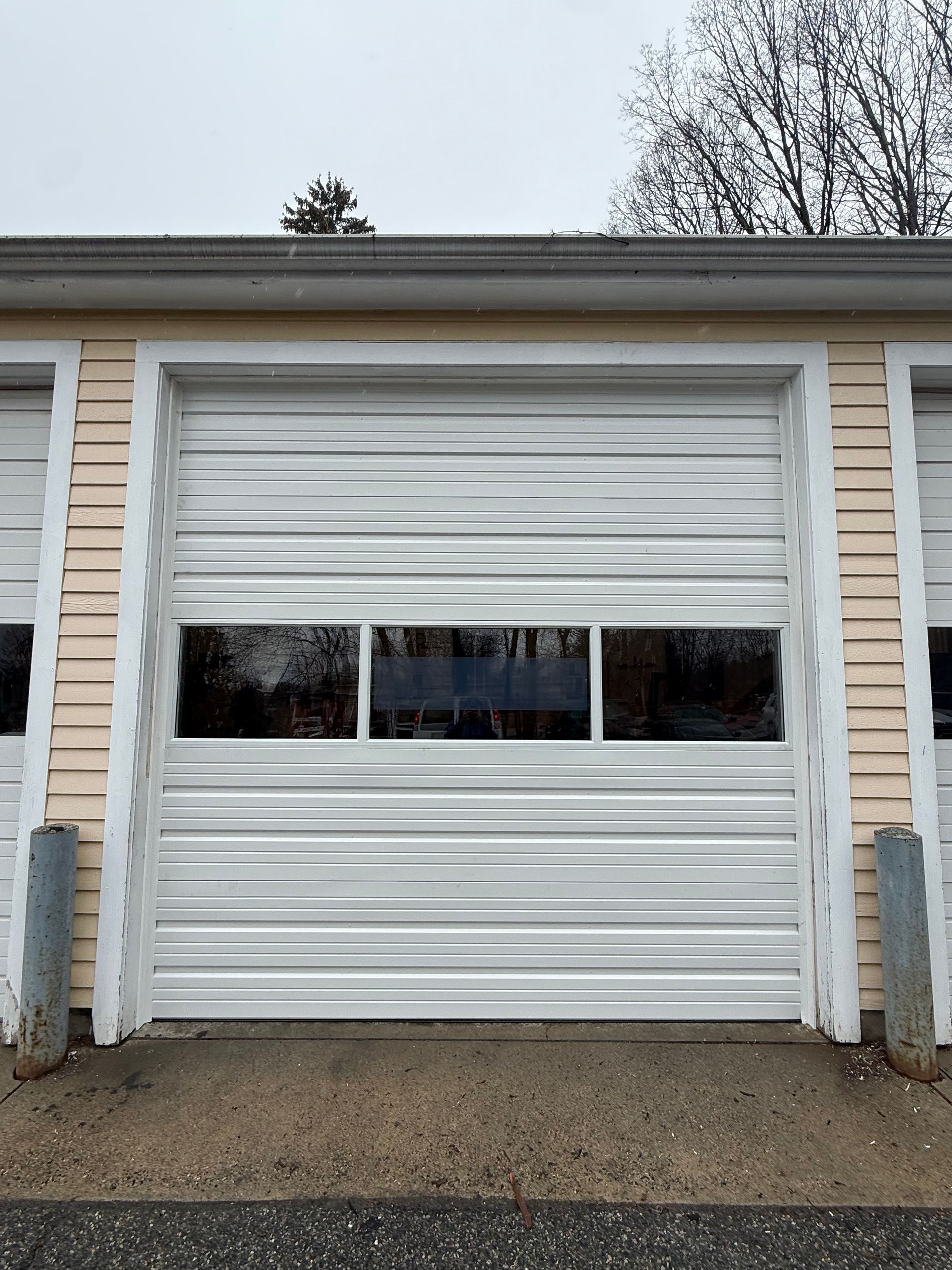 A white sectional garage door with a central row of three windows, framed by light-colored siding.