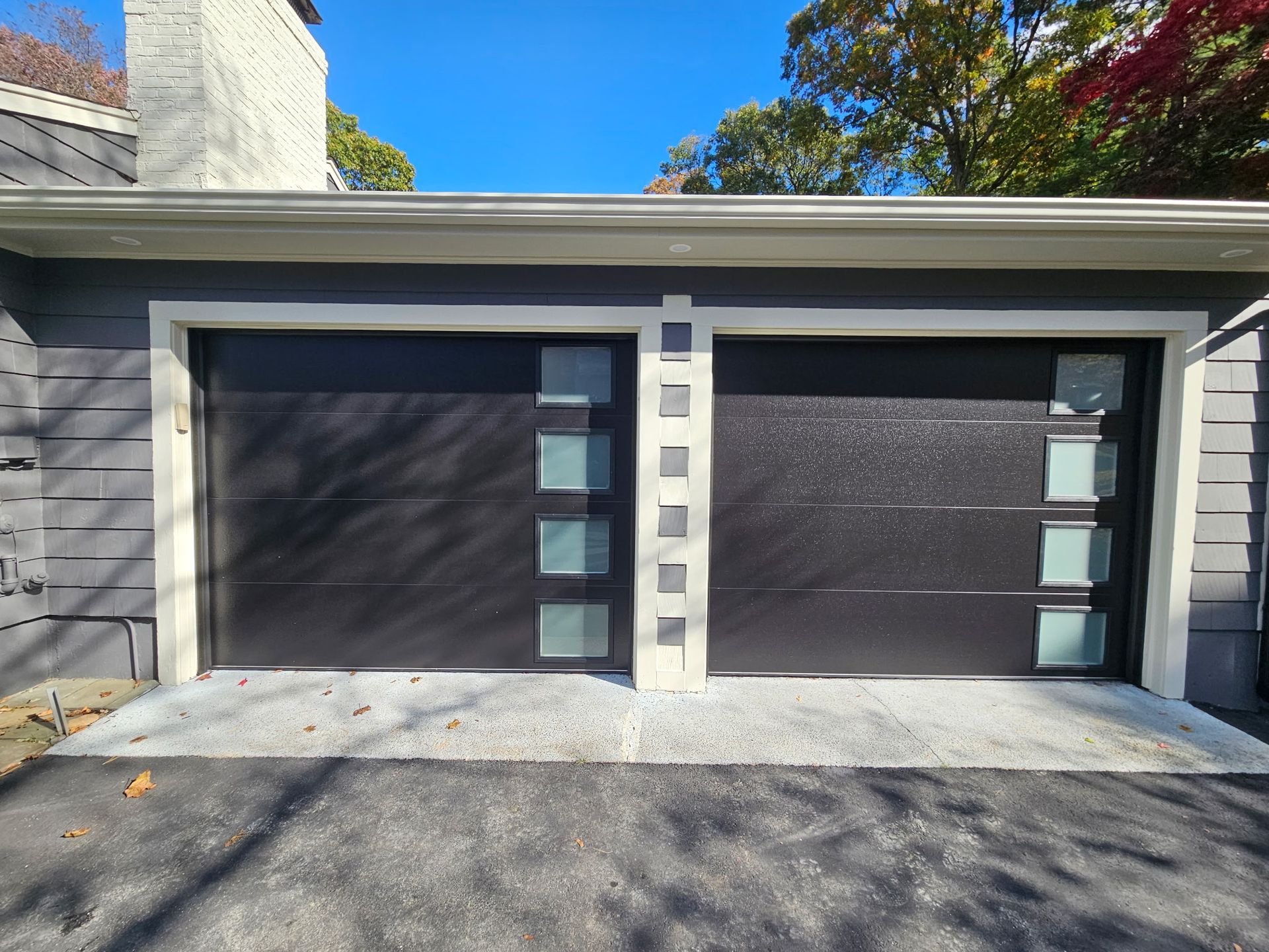 Modern home garage with two dark doors and light stone accents under a blue sky