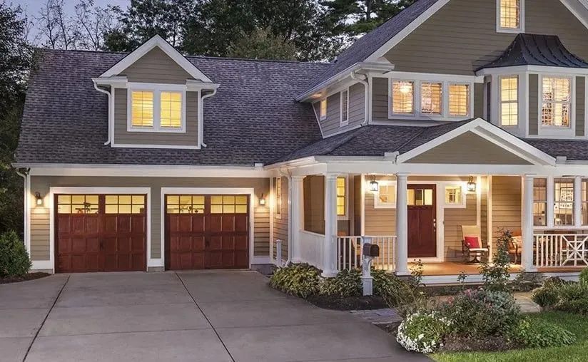 Two-story home with olive siding, dark wood garage doors, and a covered front porch, seen from a paved driveway.