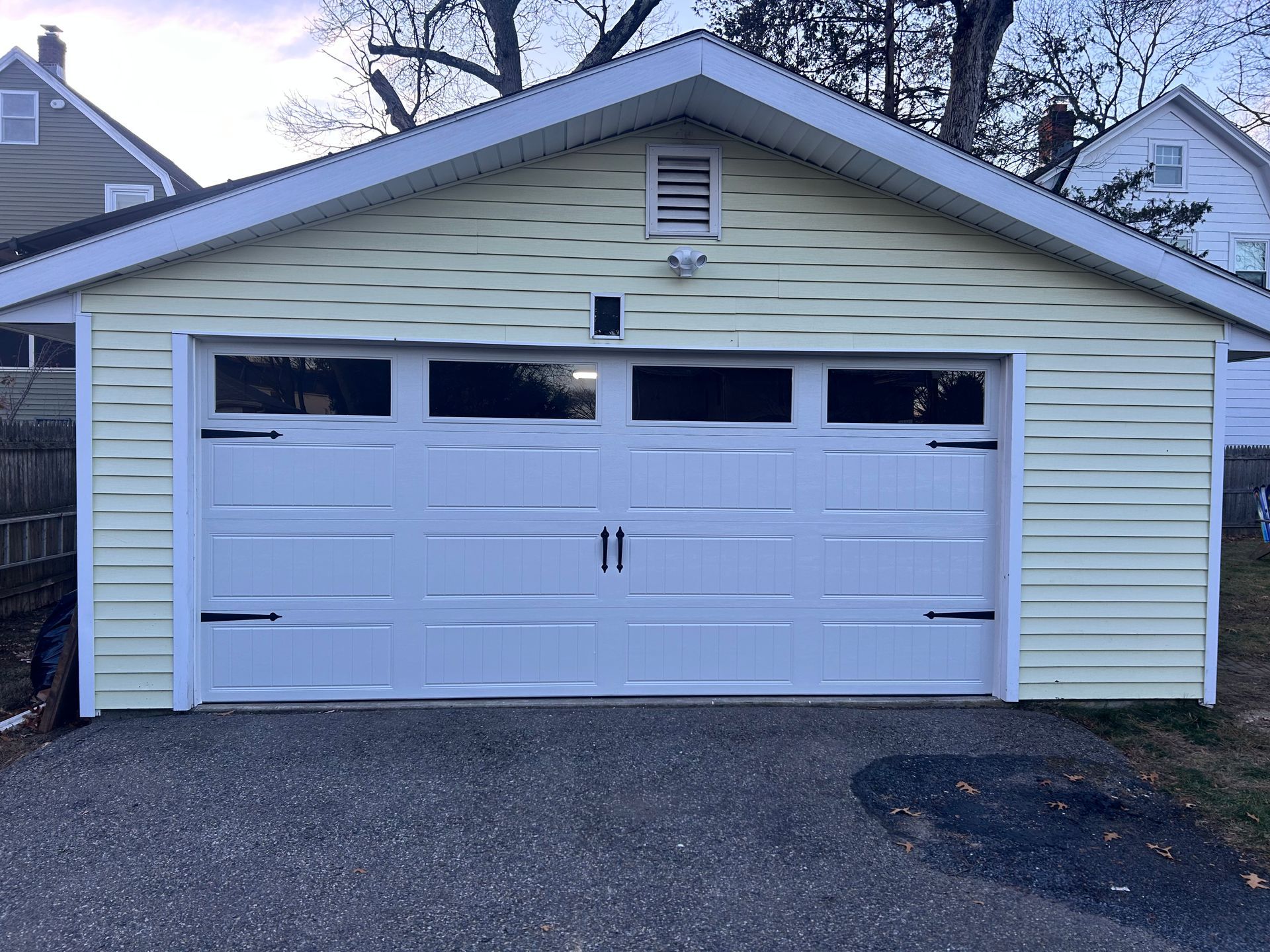 A detached, light yellow garage with a white, single-car sectional door featuring small top windows and black hinges.