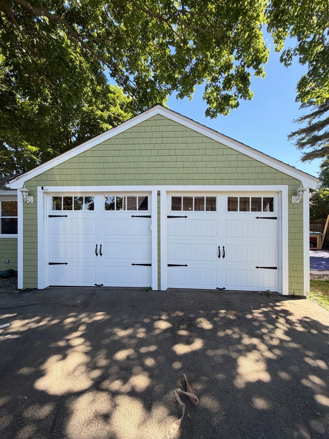 Two white garage doors on a light green detached garage under leafy trees