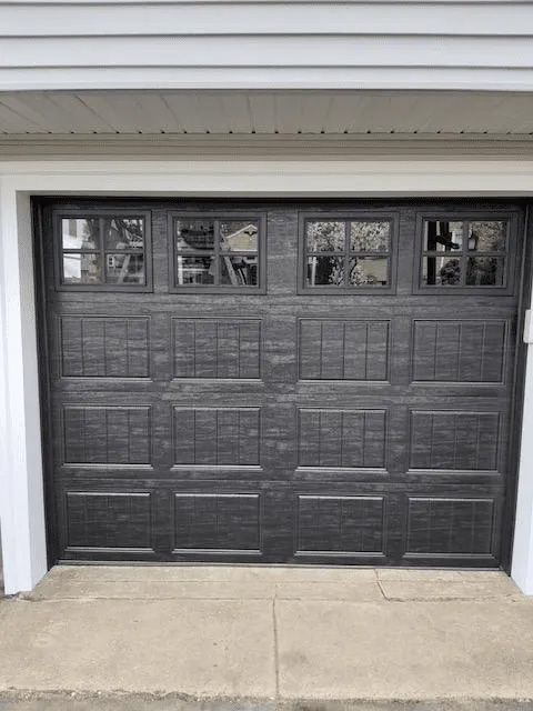 A black, paneled residential garage door with a row of four square windows across the top.