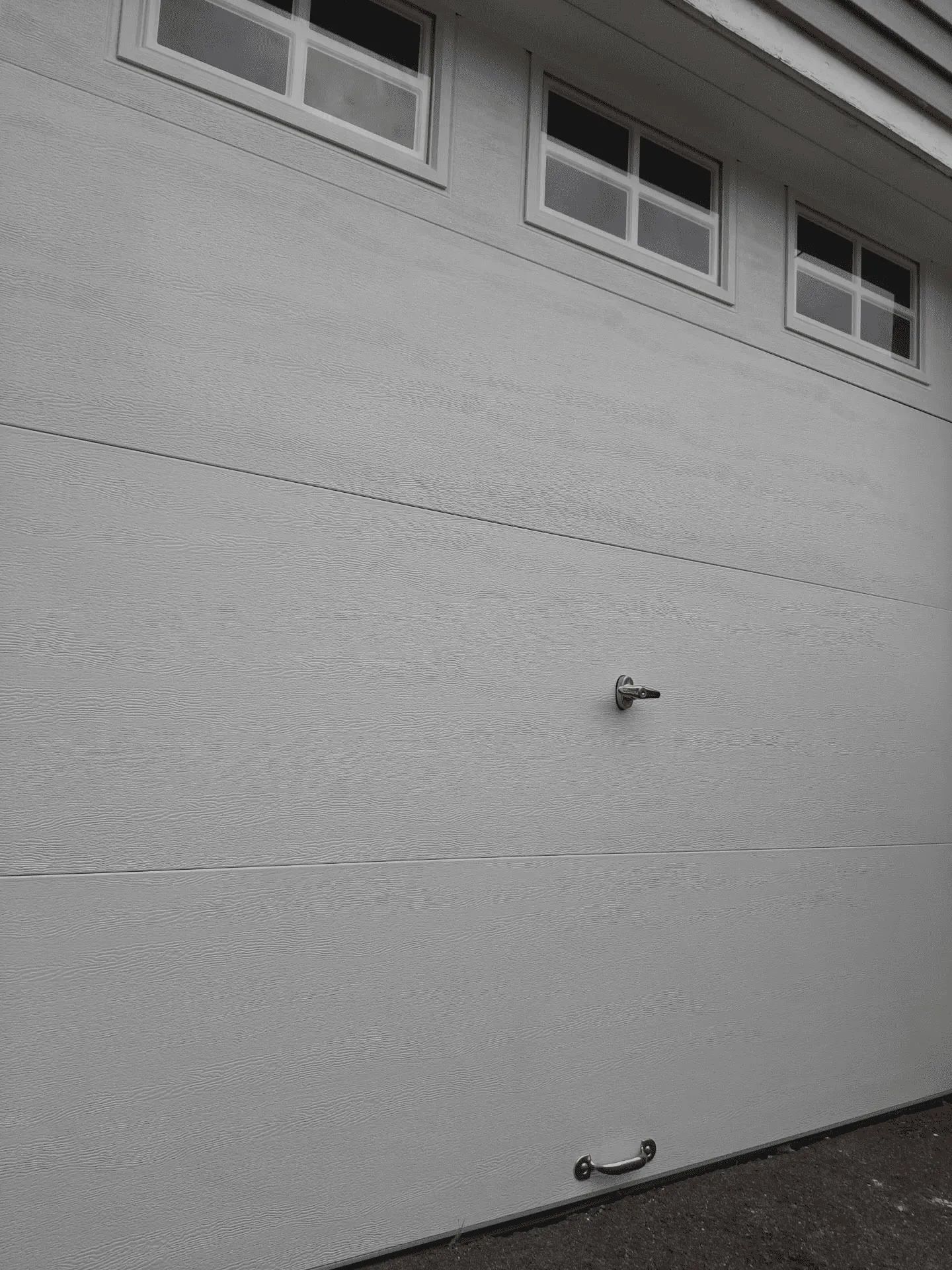 A white, textured garage door with three small rectangular windows along the top, a central lock, and a bottom handle.