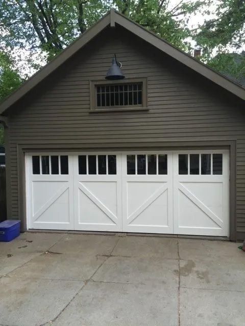 A dark brown detached garage with a white, four-panel carriage-style door and a small vent under a peak roof.