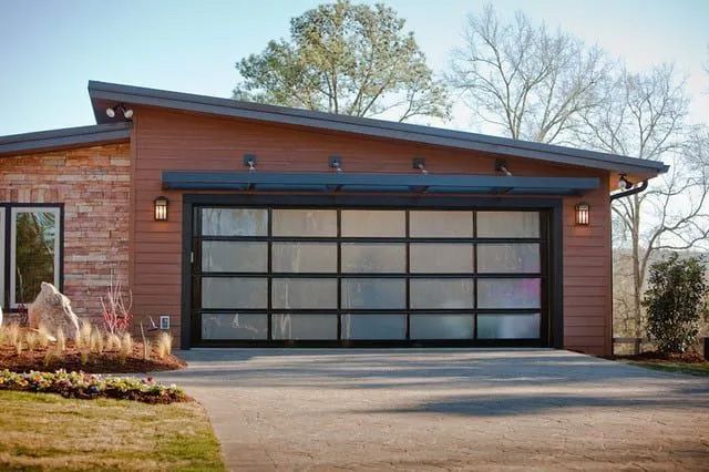 Modern garage with a multi-panel frosted glass door and wood siding, set against a background of trees.