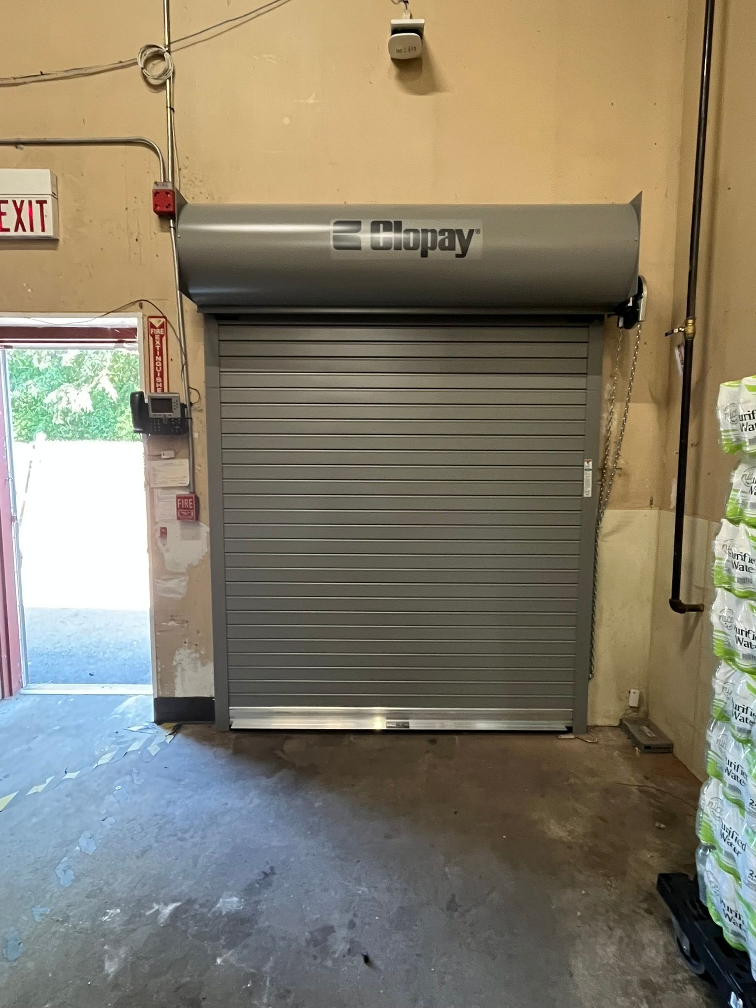 Closed silver roll-up garage door in an indoor loading area with an open doorway on the left.