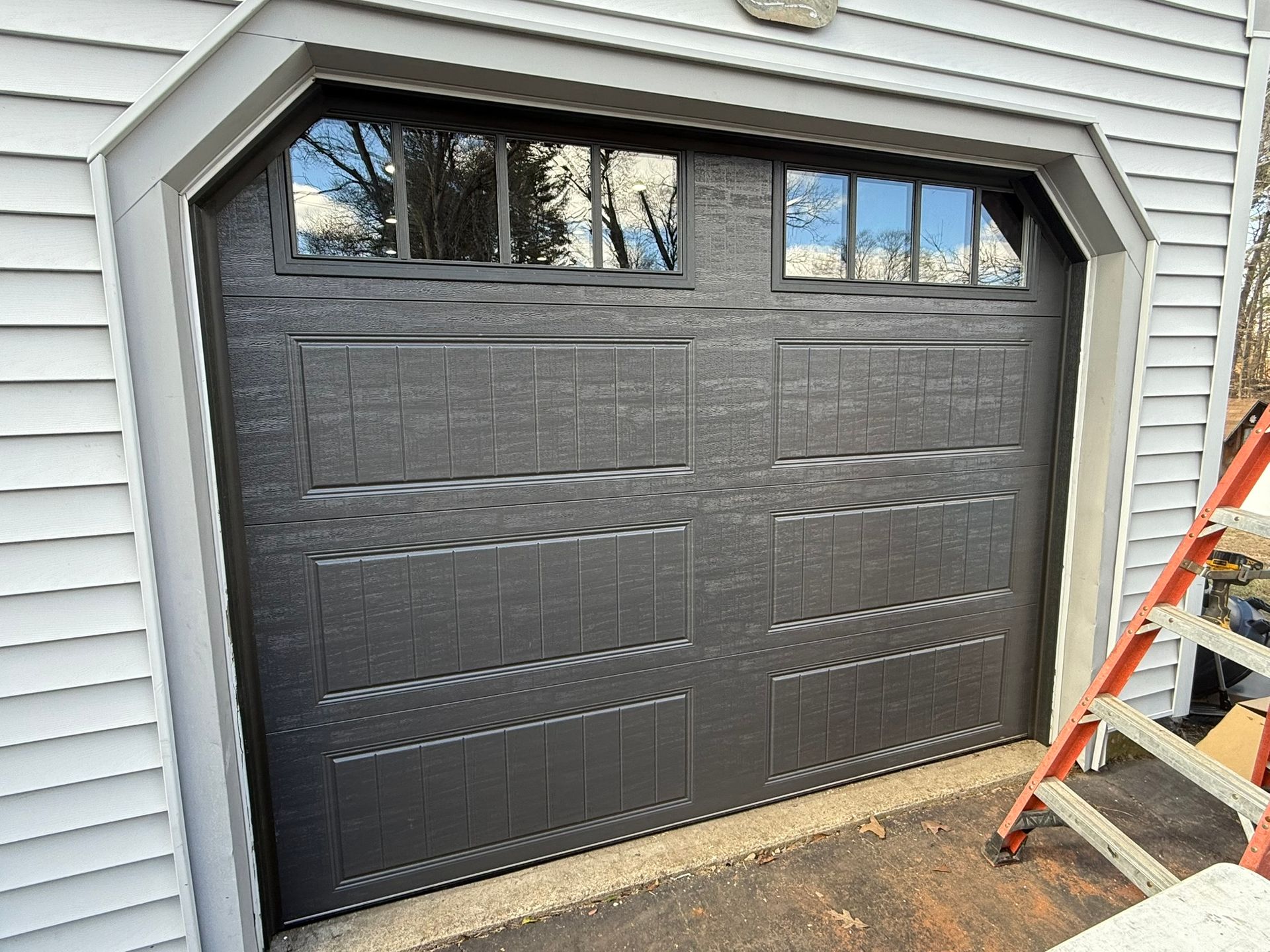 Black double garage door on a house with a step ladder beside it