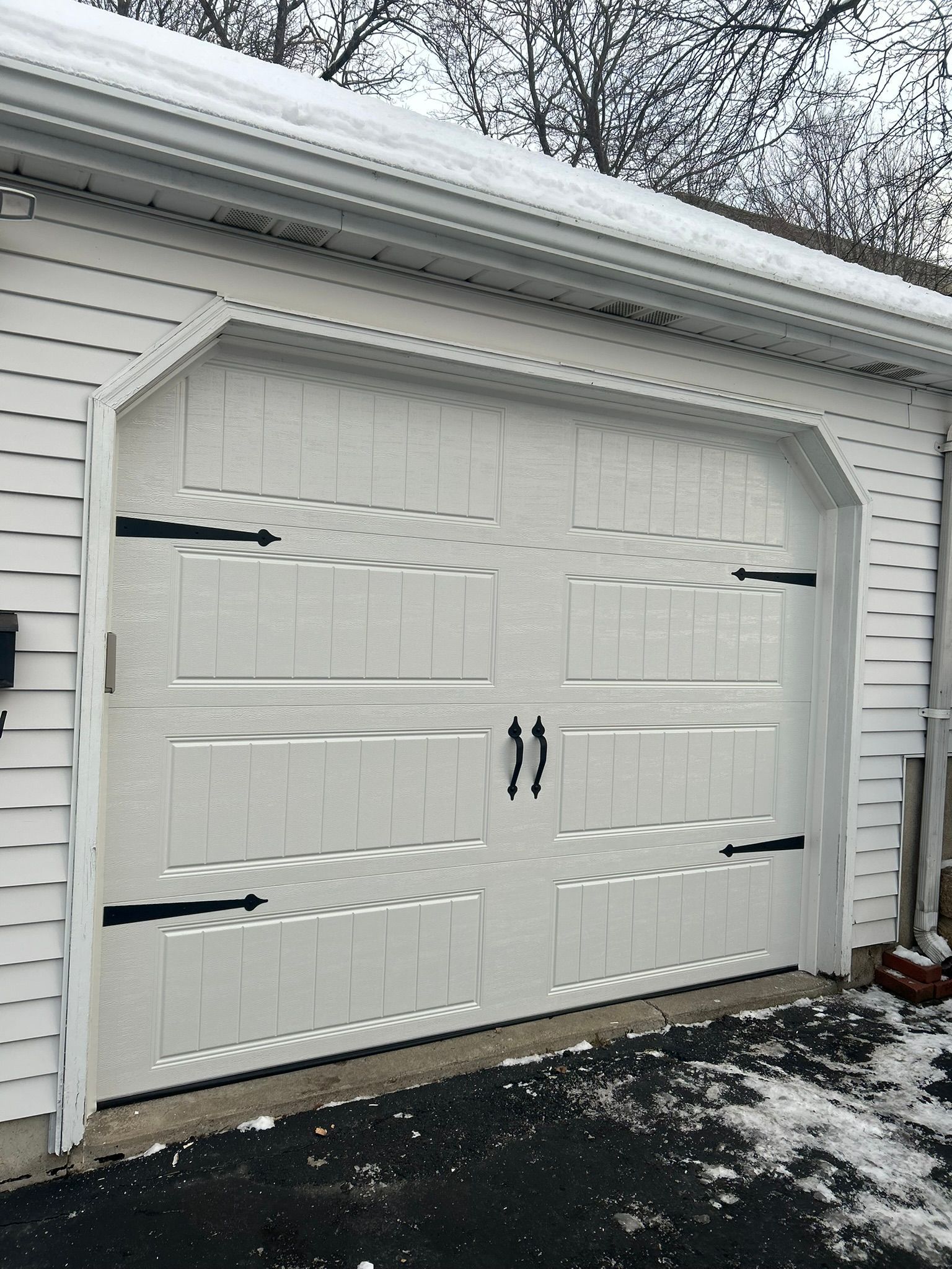 White double garage door with black handles on a snow-dusted house exterior