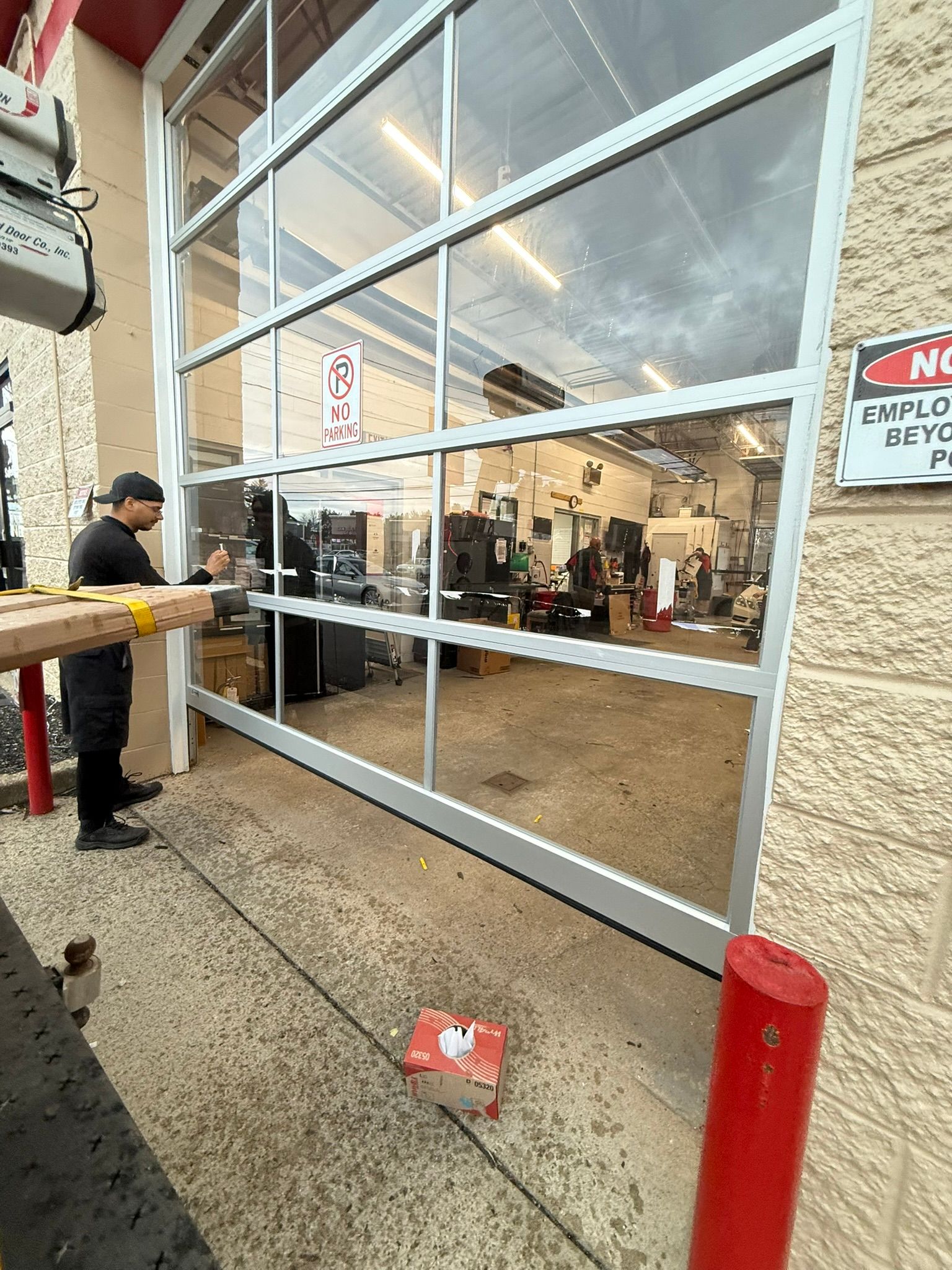Storefront entrance with large glass doors, interior visible, and a person standing outside near a red bollard.