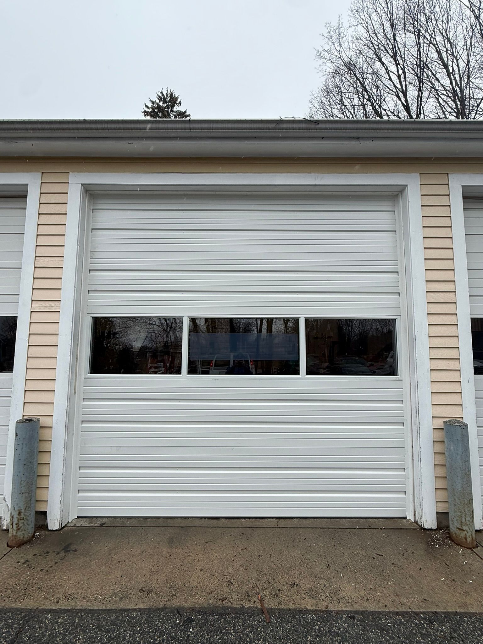 White garage door with a small horizontal window on a beige building exterior.