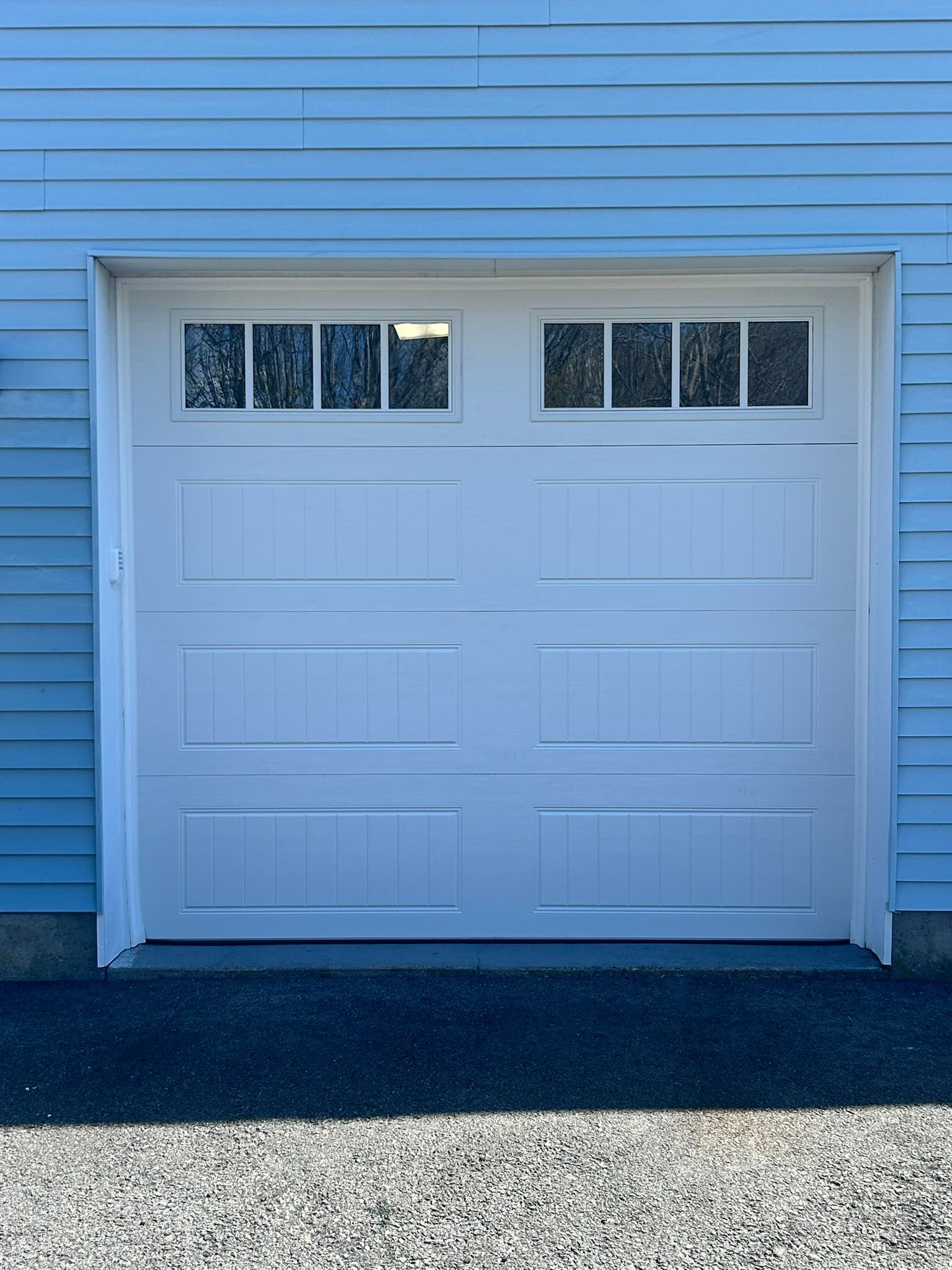 White garage door on a blue-sided house with small windows at the top.
