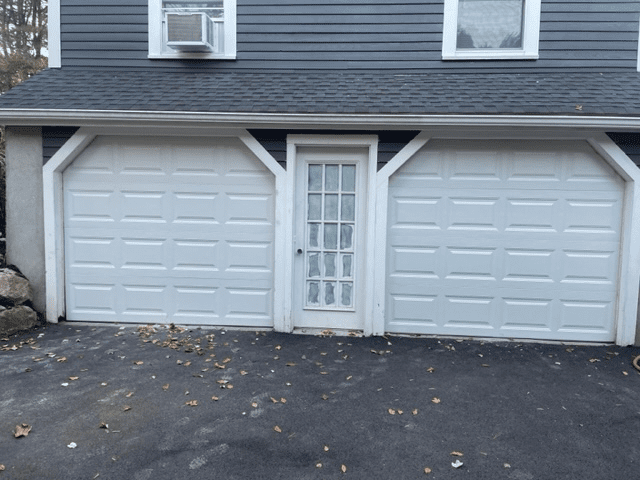 A detached garage with two white paneled doors flanking a central white pedestrian door, under blue siding.