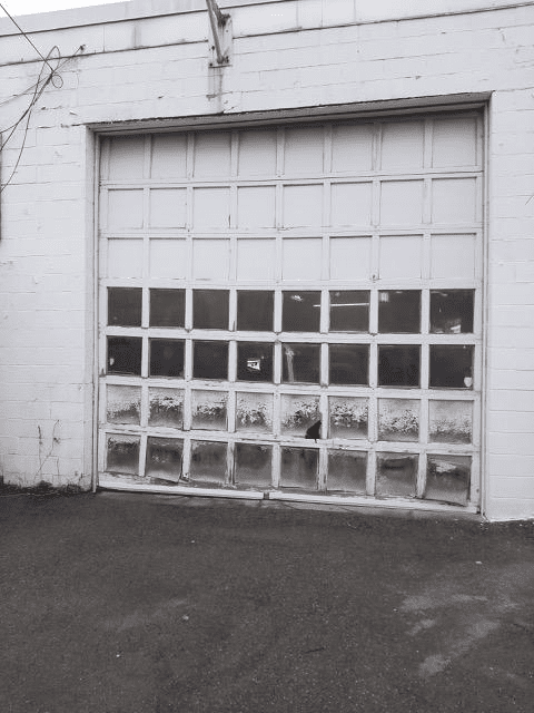 A white, multi-paneled garage door with windows on its lower half, set into a white brick wall.