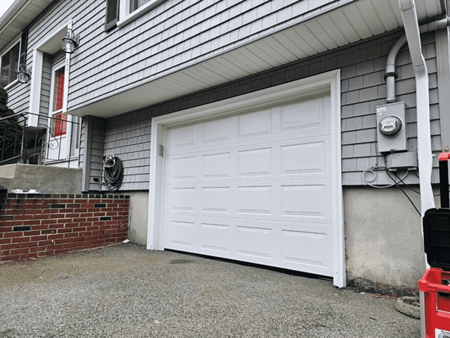 A white garage door on a house with gray vinyl siding, a brick retaining wall, and a gray gravel driveway.
