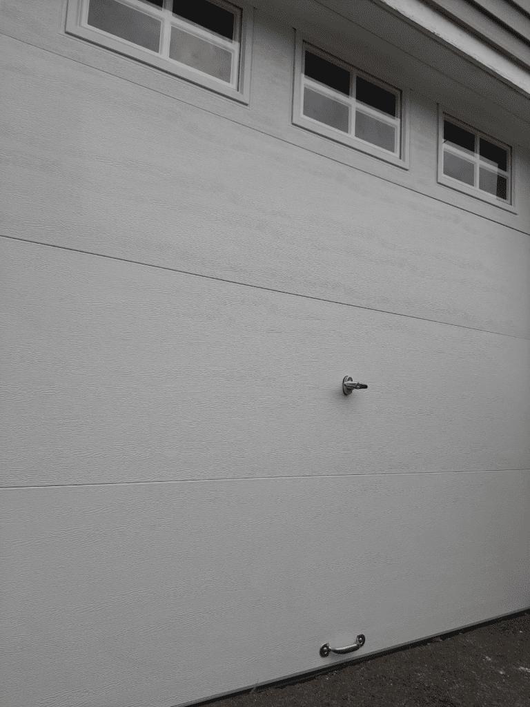 A white, textured garage door with three small top windows, a center handle, and a bottom handle.