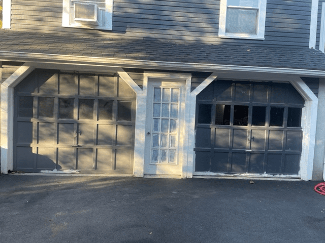 A two-story dark blue building with two garage doors and a central glass-paneled door on the ground floor.