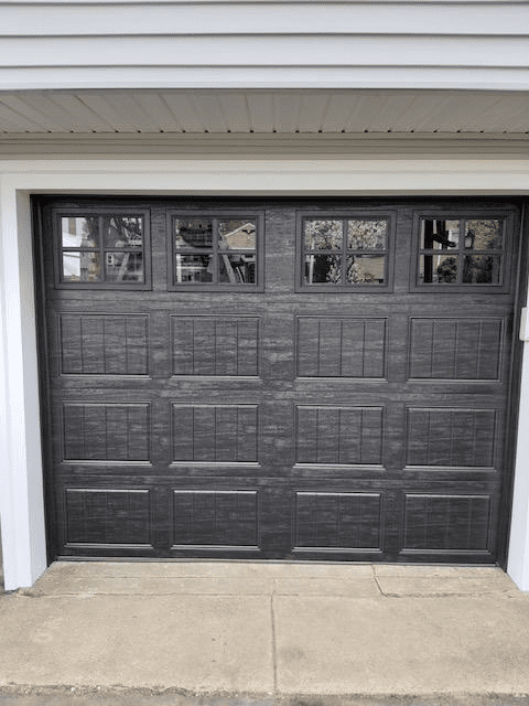 Dark-colored garage door with four rectangular windows at the top, installed in a white-trimmed frame.