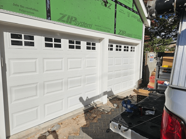 Two newly installed white garage doors with windows, set in a building framed with green ZIP System sheathing.