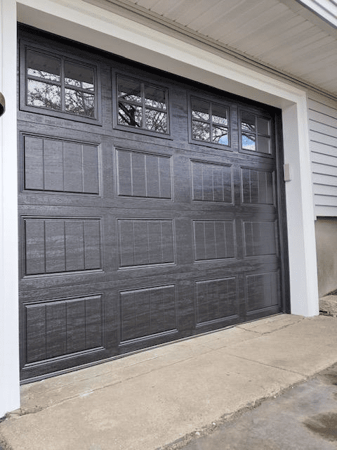 A dark gray, three-panel garage door with windows in the top section, installed in a home exterior frame.