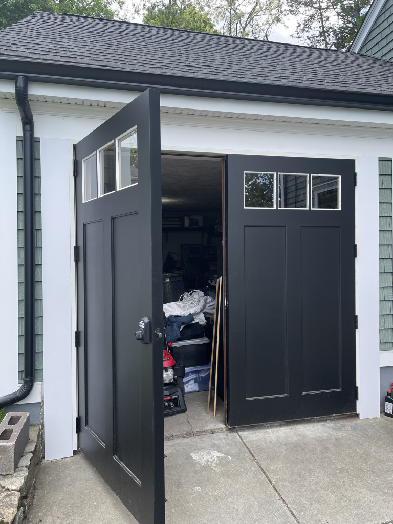 A pair of open, matte black double doors with three small glass windows at the top, installed on a white-trimmed building.