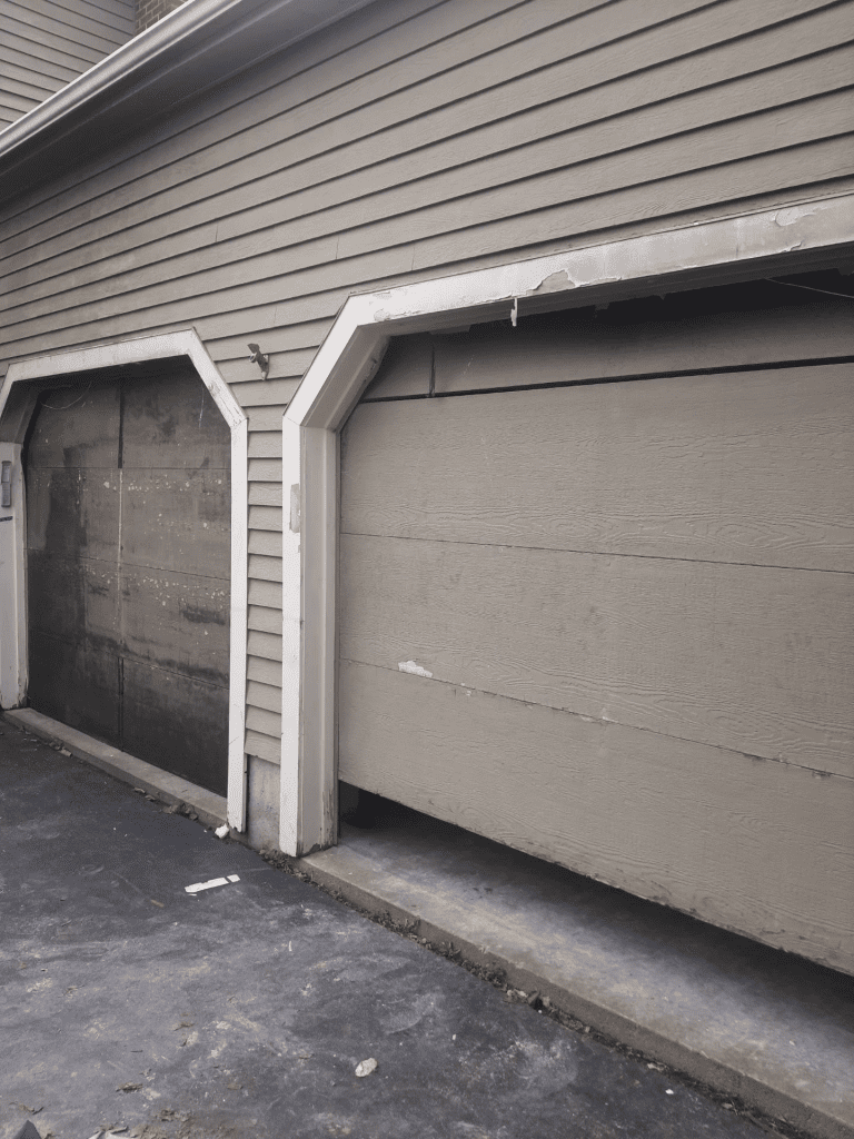 Two beige garage doors on a residential building, with the right door partially raised, revealing a gap at the bottom.
