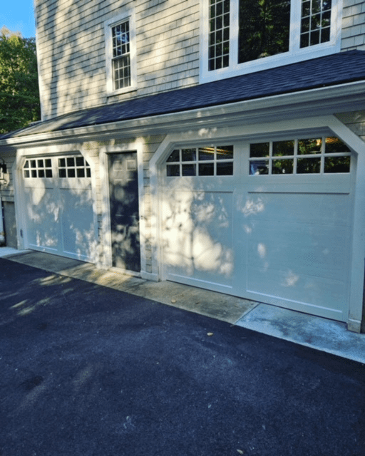 A two-car garage with white paneled doors featuring top window rows, separated by a dark gray pedestrian door.