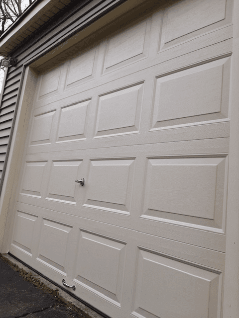 A beige, paneled garage door viewed from an angle against gray siding.