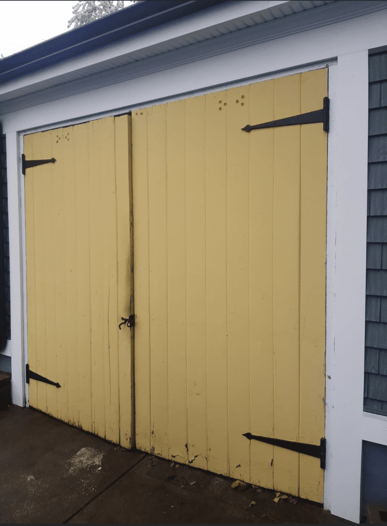 A pair of tall, vertical-planked yellow garage doors with black decorative strap hinges, set in a white frame.