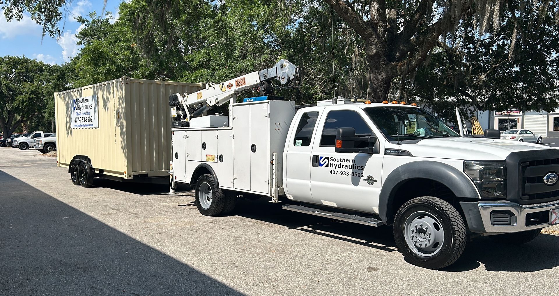 A white truck with a trailer attached to it is parked on the side of the road.