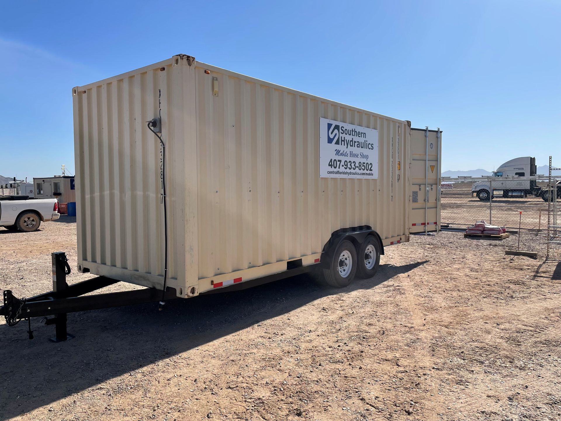 A shipping container on a trailer is parked in a dirt field.