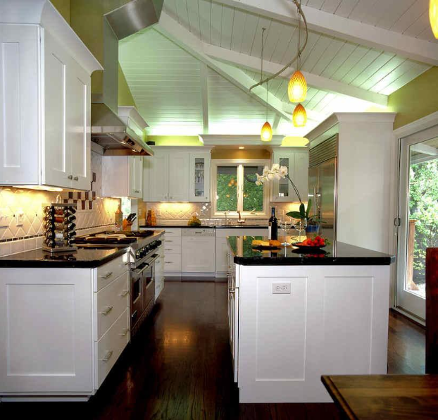 White kitchen with black countertops, wood floor, vaulted ceiling, and pendant lights.