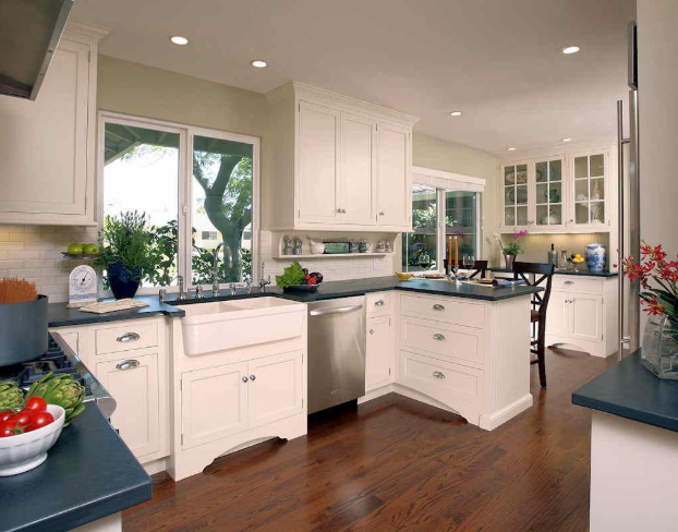 White kitchen with dark countertops, wooden floors, and a farmhouse sink.
