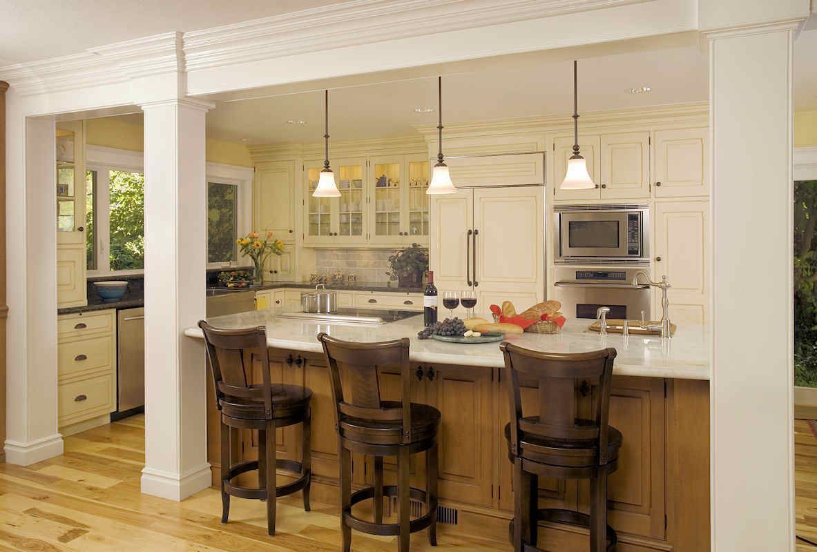Kitchen with island, light wood cabinets and floor, white countertop, bar stools, and pendant lights.
