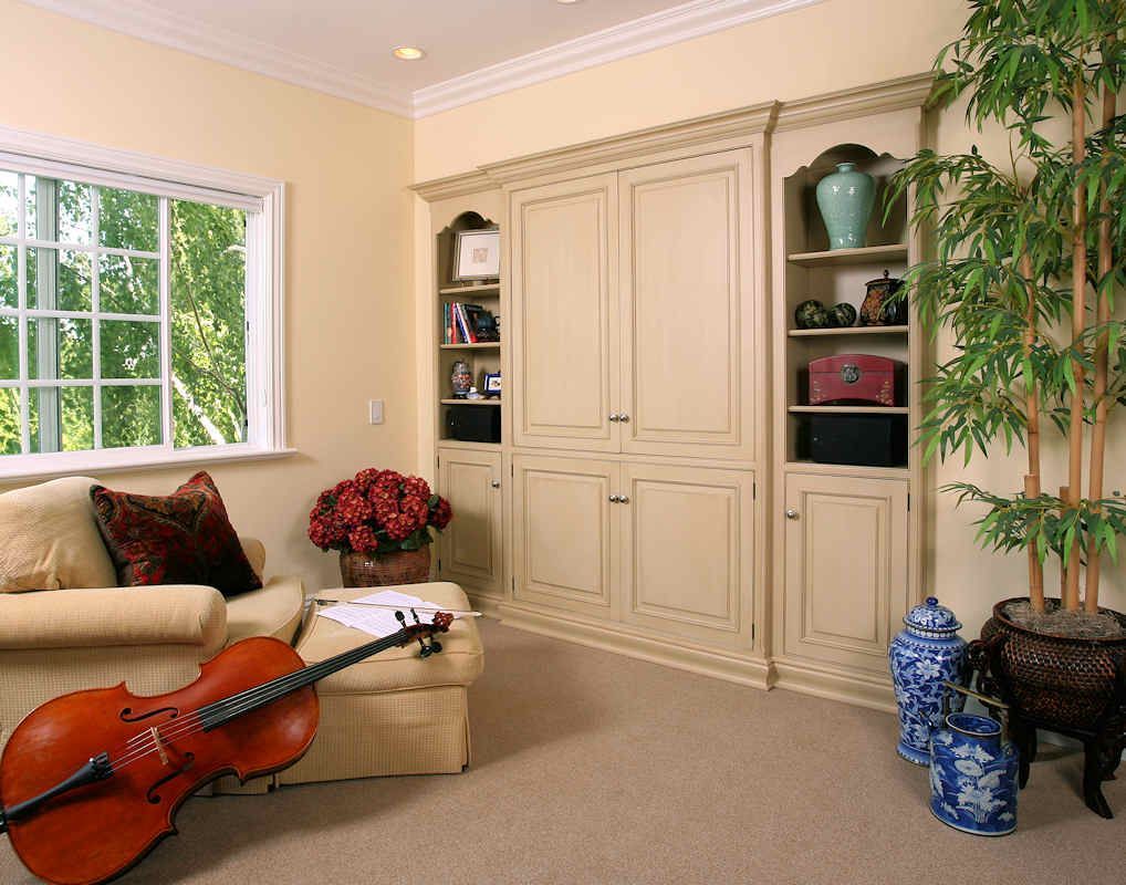 Cello in a cozy room with built-in storage, a window, and a bamboo plant. Beige and cream tones dominate.