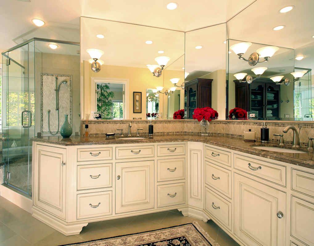 Elegant white bathroom with granite countertop, large mirrors, glass shower, and vanity cabinets.