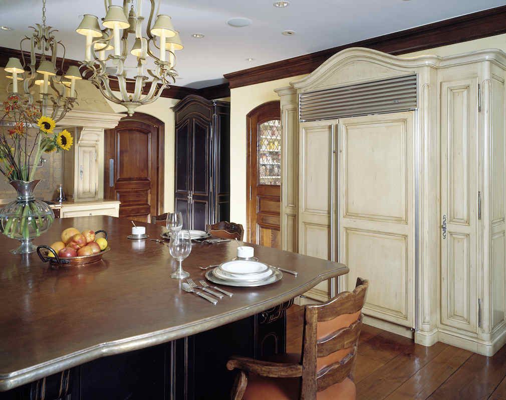 Kitchen with large wooden island, cream-colored cabinets, chandelier, and seated chair at island.