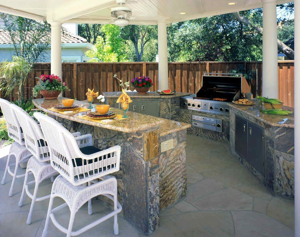 Outdoor kitchen with granite countertops, grill, and bar seating under a covered patio.