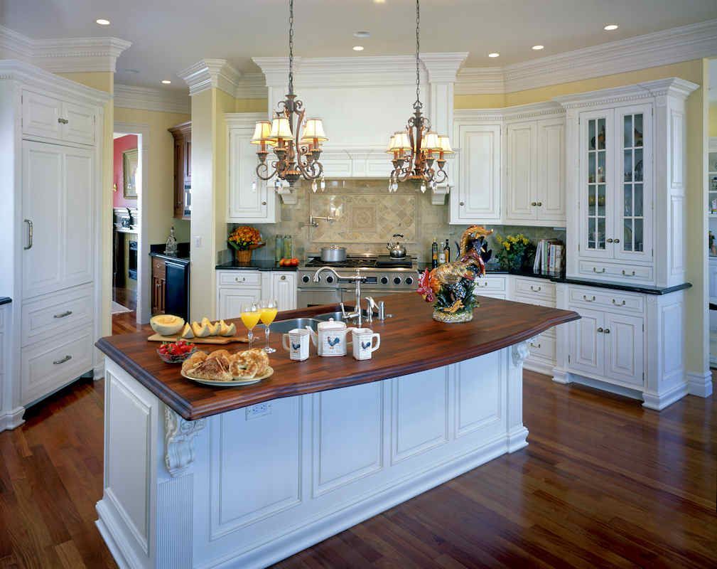 Elegant white kitchen with wooden floors, island, cabinets, and two chandeliers.