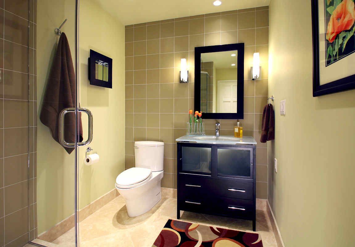Modern bathroom with a glass shower, toilet, dark vanity, and neutral-toned tiles.