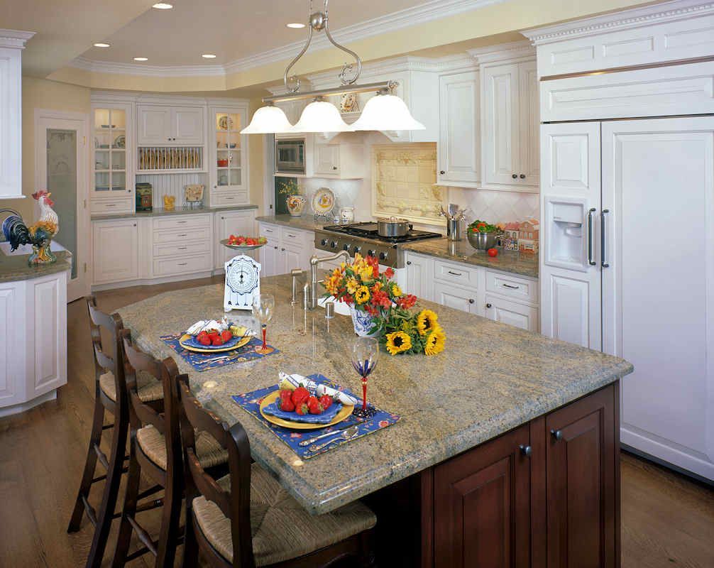Kitchen with white cabinets, brown island, granite countertops, and wooden chairs.