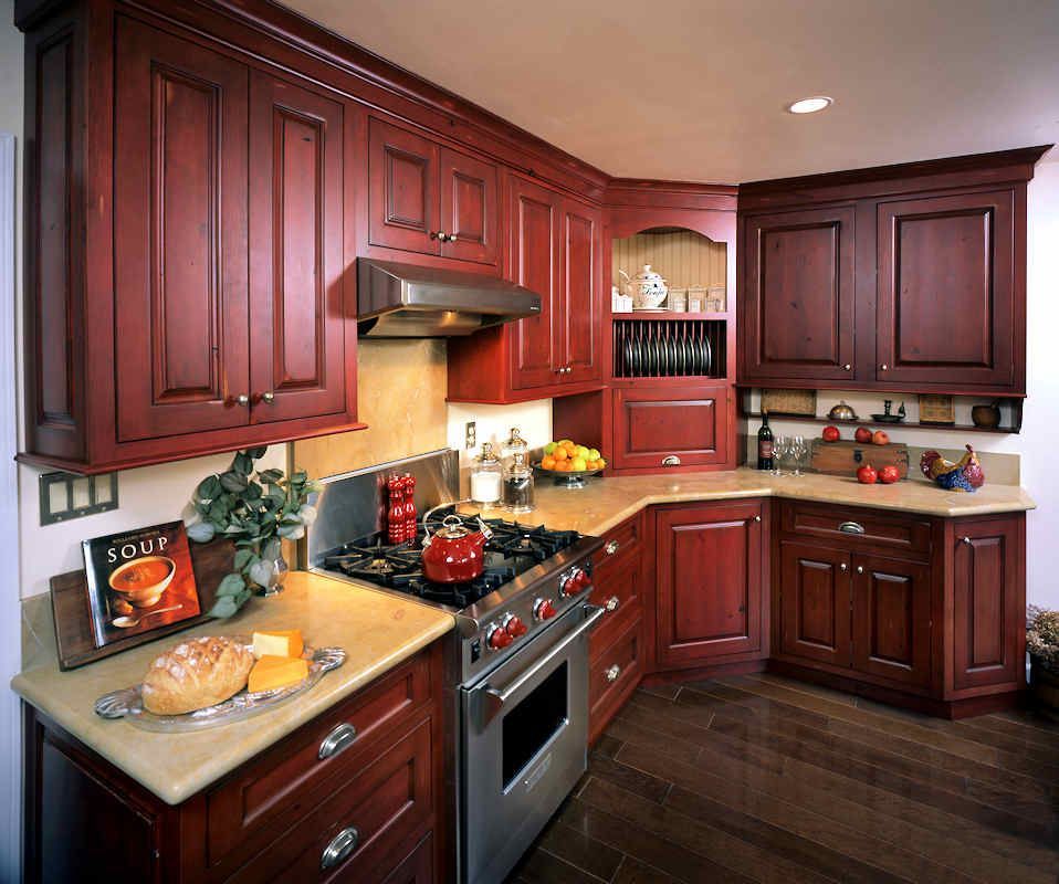Reddish-brown kitchen cabinets surround a stainless steel range and beige countertops.