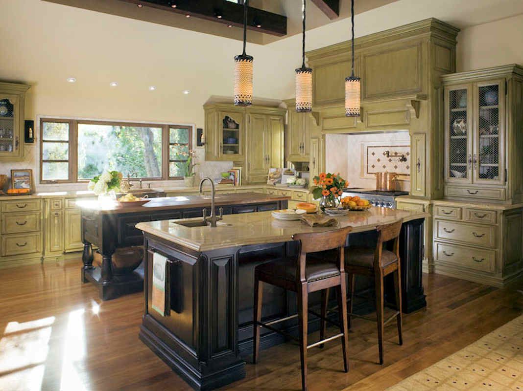 Spacious kitchen with two islands, green cabinets, dark brown accents, and wooden floors.