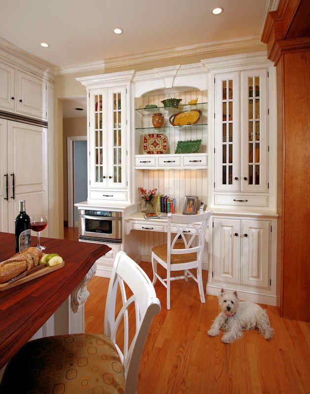 White kitchen with built-in desk, cabinets, and small dog on the wooden floor.