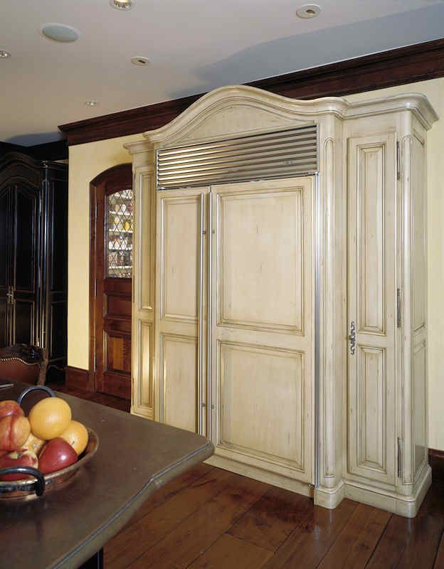 Built-in refrigerator with cream-colored distressed cabinet doors in a kitchen; wood floor.
