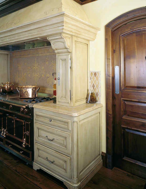 Kitchen with cream-colored cabinetry, drawers, stove, and a dark wooden door.